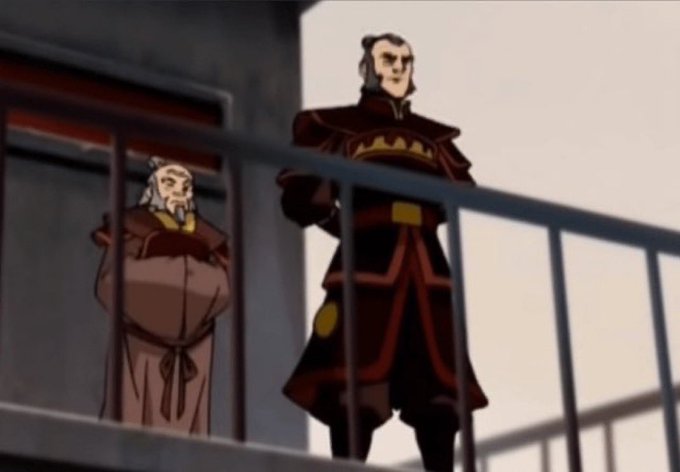 A screenshot from an animated show featuring two characters in dark red robes standing on a balcony, with a tall man in fire nation attire and an older man with white hair and beard in the background.