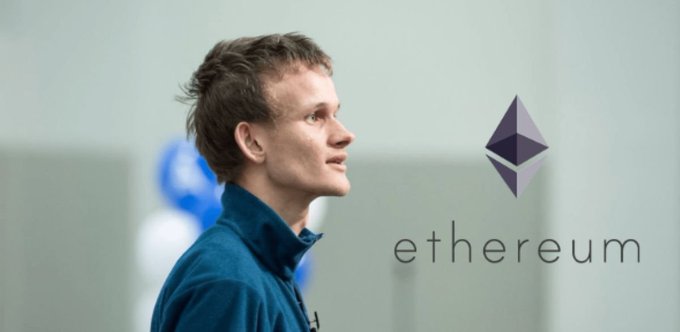 In the image, a man wearing a blue jacket stands next to a large banner with the word "ETHEREUM" written on it. The man has short hair and seems to be looking off to the side as if observing something or someone outside of the frame. The backdrop is a white wall that appears to be part of a room or indoor space, adding to the overall atmosphere of the scene. There are no visible texts or logos other than "ETHEREUM" on the banner, and no objects like chairs or suitcases in the immediate vicinity. The man wearing the blue jacket seems to be the main subject of this image.