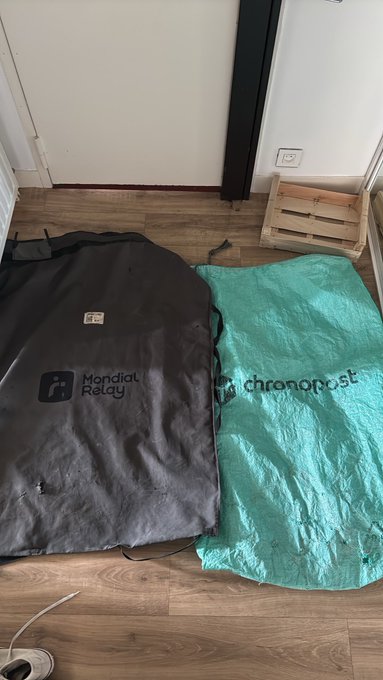 Two bags lie on a wooden floor: a black cover with "Mondial Relay" branding and a teal bag labeled "chronopost."