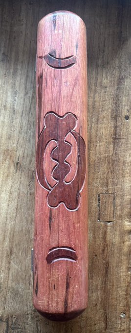 A close-up shot shows a carved wooden object featuring an abstract, symmetrical knot design resting on a wooden surface.