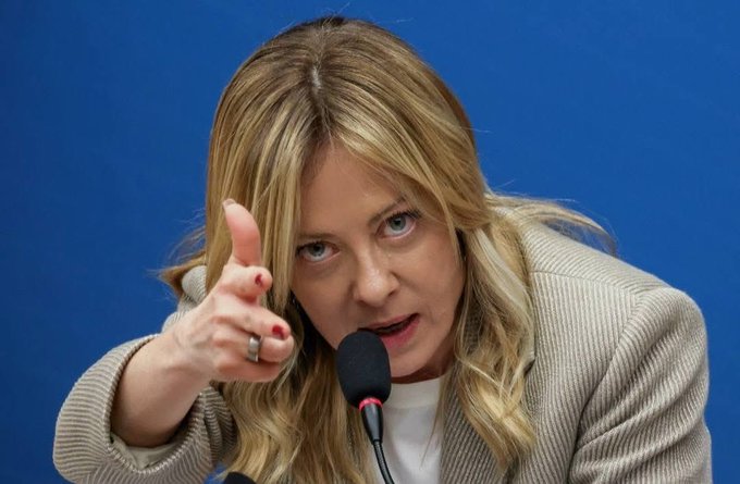 The image shows a woman wearing a beige jacket with her hand raised up, possibly pointing or gesturing towards something. The background of the image is blue, which contrasts with the white text that reads "Banca Sella" on the right side. This suggests that the image might be related to a news article about Banca Sella becoming the first Italian bank to offer Bitcoin and cryptocurrency services.