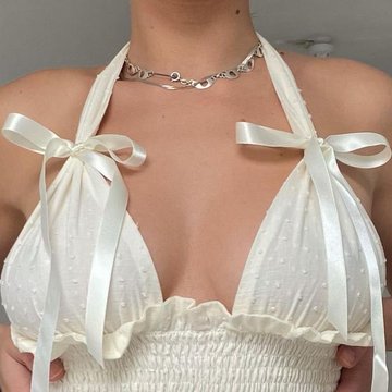 A close-up photo showing a woman wearing a white halter top with bow details and a silver chain necklace.
