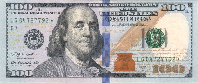 The back side of a US $100 Federal Reserve Note featuring Benjamin Franklin's portrait, serial number LG 04727792*, with a distinctive blue vertical security ribbon.