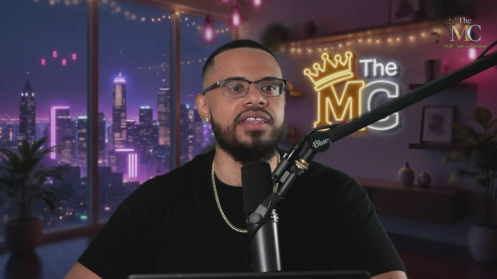 The image features a man wearing glasses, sitting at a desk with a microphone attached to his microphone stand. He appears to be talking into the microphone during an interview or discussion about the top memes being shared online. The background of the image shows a city skyline, indicating that they are likely discussing this topic in a public setting like a podcast studio or a live event broadcasted on television.