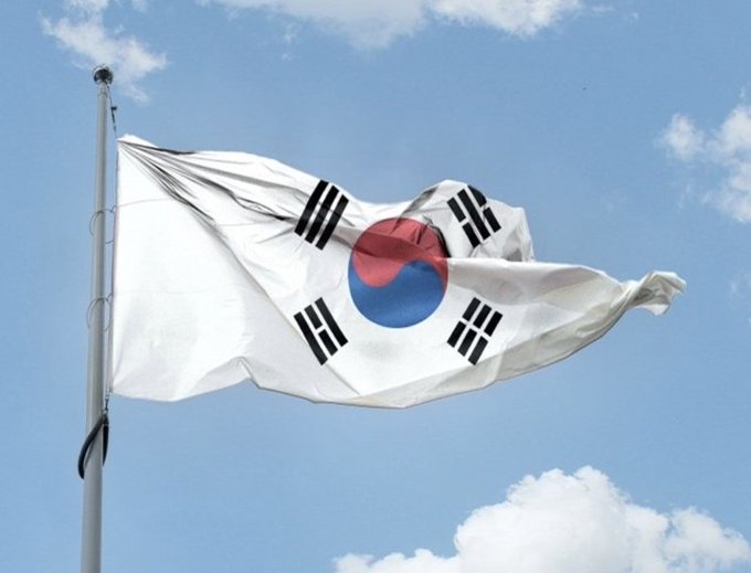 The flag of South Korea, with its distinctive Taegeuk symbol and four black trigrams, waves against a blue sky, representing the country actively investigating 30 crypto market manipulation cases under its new regulatory framework.