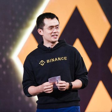 A man wearing a black "BINANCE" hoodie speaks on stage while holding cards, as the founder/chairman of the cryptocurrency exchange Binance. The image ties to the post's message about prioritizing market resilience and longevity over superficial thrills like fast vehicles.
