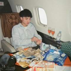 A man sits in a private jet surrounded by stacks of cash, wallets, bottles, and packaged items. The image appears illustrative of the accompanying post’s claim about a wallet profiting roughly $26K from buying and quickly selling $KIMCHI tokens.
