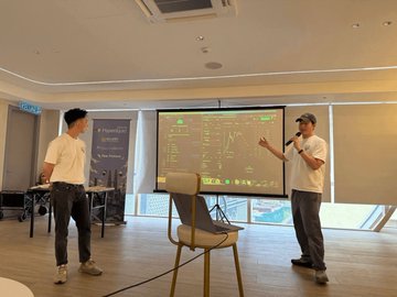 Two men giving a presentation in front of a projection screen displaying a diagram with multiple boxes and arrows in a conference room.