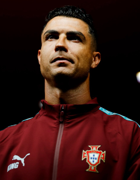 Cristiano Ronaldo gazes upward with a focused expression, wearing the red Portugal national team training jacket featuring the Puma logo and Portuguese crest. The image embodies the "sacred mortal" warrior of the Portuguese Dynasty, capturing the determined spirit of a legendary football cultivator poised for battle.