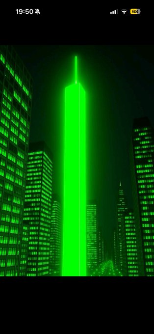 A nighttime cityscape featuring a tall skyscraper illuminated in bright green light, viewed on a mobile phone screenshot.