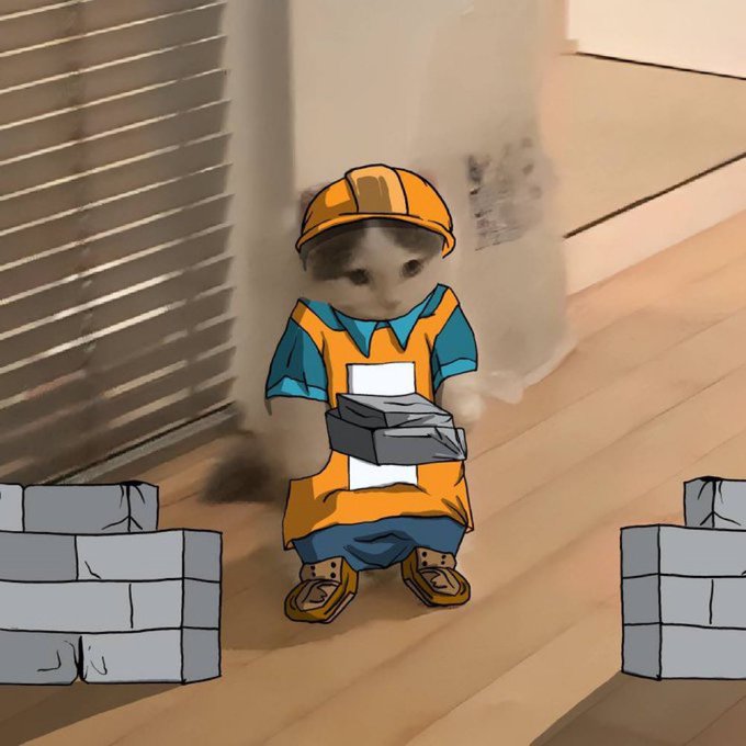 A digitally edited image shows a kitten wearing an animated orange hard hat and safety vest, holding a small gray brick, placed among cartoon stacks of bricks on a wooden floor.