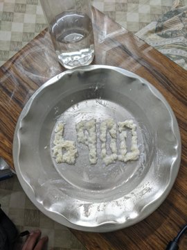 A metal plate on a wooden table with the word 'END' spelled out in a grainy substance, next to a glass of water.