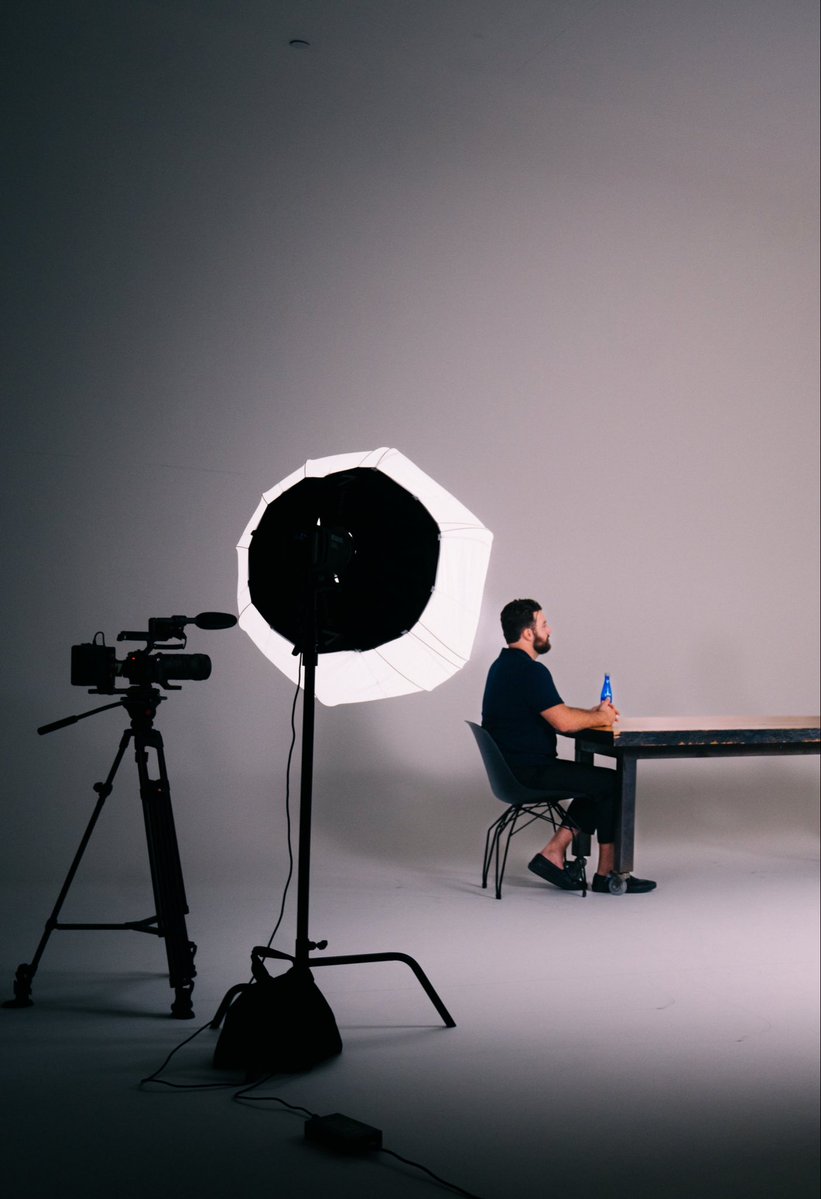A behind-the-scenes photo studio setup reveals a man sitting at a table with a blue Stabledash bottle, illuminated by a large octagonal softbox light while a video camera on a tripod records the scene—visually emphasizing that there's "so much more to Stabledash than meets the eye" beyond what audiences see in the final footage.