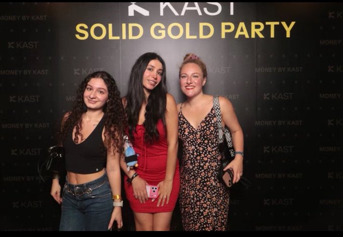 Three women posing in front of a backdrop that reads "KAST SOLID GOLD PARTY" and "MONEY BY KAST" at what appears to be a branded event.