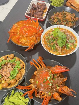 A spread of Chinese dishes featuring a large spicy crab, braised beef, edamame, and a bowl of soup or stew on a dark table.