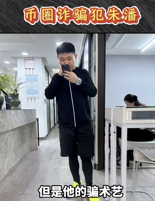 The image features a man taking a selfie with his phone while standing in an office setting. The photo captures him wearing black shorts and a black jacket as he poses for the picture. The background of the image shows a desk, chair, potted plant, and a vase on the floor. There is also text present in the image that reads "spread the word spread the word He Yi @binance @binance officials Zhu Pan once impersonated others in an attempt to scam her, which failed, and even impersonated himself to scam Justin Sun @justinsuntron".