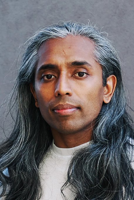 A man with long, graying hair and a serious expression gazes directly at the camera against a neutral gray background. The post's reference to "time is a flat circle" suggests the portrait's timeless quality and the subject's weathered, reflective appearance evoke a sense of cyclical inevitability and enduring presence.