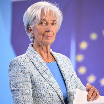Christine Lagarde, the President of the European Central Bank, wearing a blue tweed jacket while standing before an EU flag.