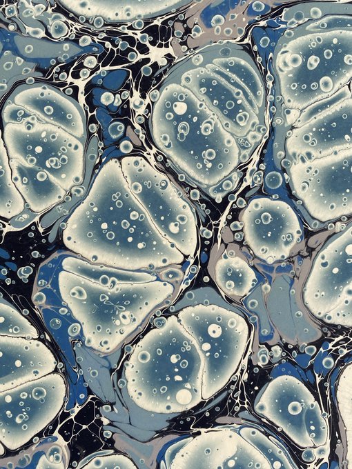 An abstract fluid art pattern featuring blue, white, and black tones with bubble-like cellular textures.