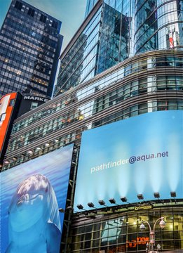 The image features a large billboard with an advertisement for Aquafind.net, which displays a picture of a dolphin along with the website's address. The text "Happy Monday! The dolphins are already showing off their aqua.net Lightning Addresses." is also present on the billboard. This advertisement seems to be promoting the website and its services related to finding lightning addresses for people who want to share their location information online.