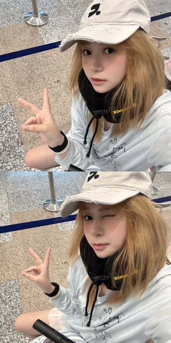 A two-panel selfie of a young woman with blonde hair wearing a beige cap, white hoodie, and headphones around her neck, posing with a peace sign in what appears to be an airport.