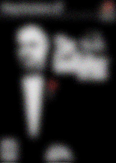 The image features a blurry photo of a man's face, with the focus being on his eyes rather than his facial features. The background appears dark, which emphasizes the subject matter. The caption "THE GODFATHER Starting bid: 1xtz" suggests that this is an advertisement or promotional material for a product or service related to the concept of timekeeping and punctuality.