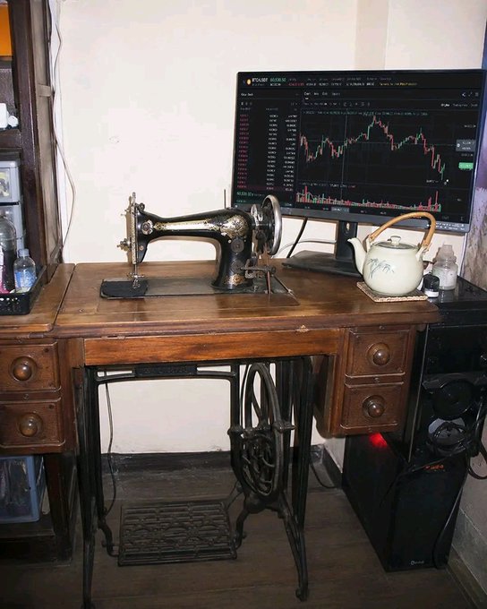 An antique black sewing machine sits atop a wooden treadle desk alongside a teapot, juxtaposed with a modern monitor displaying a stock/crypto trading chart (showing BTCUSDT Perpetual and SOLUSDT Perpetual pairs) — a fitting visual for "Grinding on Grandma's setup while keeping an eye on @wallchain," blending old-school craftsmanship with modern crypto trading.