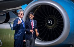 Secretary of State John Kerry and another man in suits walk in front of a massive jet engine, with the image used to visually reference "X. R. P." as an acronym play on "State Department" or diplomatic air travel.