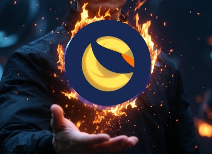 The image features a person's hand holding a fire-like object with a yellow circle and blue logo on it. The background of the image is dark and has sparks flying out, creating an intense atmosphere. The caption for this image reads "LUNC quietly climbing while most timelines are distracted elsewhere Higher lows. Volume returning. Community still one of the strongest in crypto." This description emphasizes the fire-like object's significance and its connection to the post about cryptocurrency.