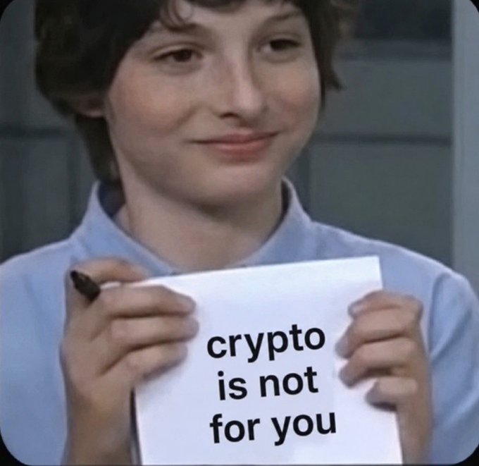 A young man with curly hair smiles while holding a sign that reads 'crypto is not for you', a popular meme image.