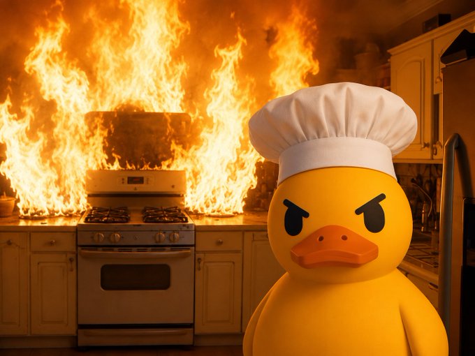 An angry yellow rubber duck wearing a white chef's hat stands in front of a kitchen with a stove engulfed in large flames.