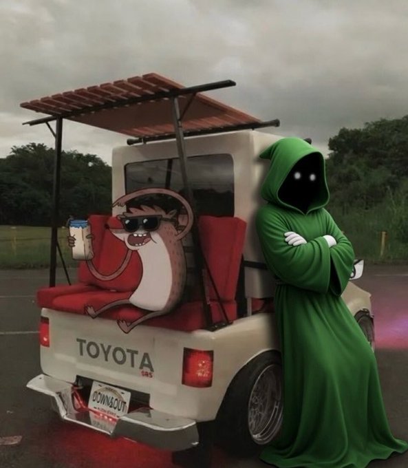 The image features a person dressed as a character from the animated series "The Simpsons" standing next to a white Toyota truck with a red roof, wearing a green robe or hooded garment. The scene appears to be set outdoors, possibly on a golf course, given that there is a golf cart in the background.