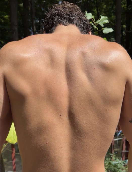 A photograph of a man's muscular back outdoors, showing defined musculature with sweat glistening on the skin.
