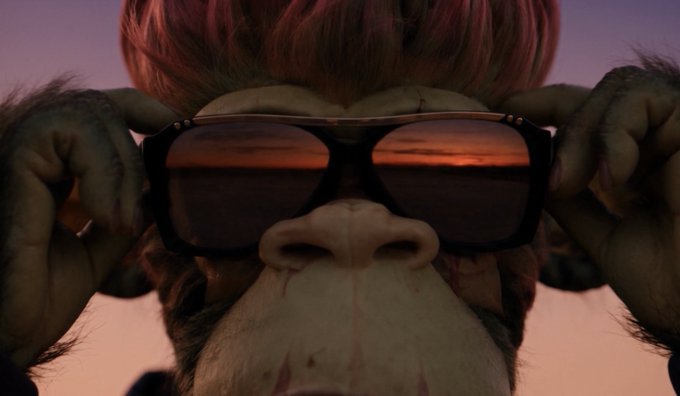 A close-up view of an anthropomorphic monkey character wearing large sunglasses that reflect a sunset over water, with the character holding the glasses in place with both hands.