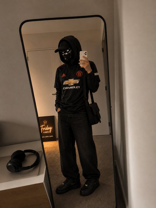 A mirror selfie shows a person wearing an all-black outfit including a Manchester United Chevrolet jersey, hood, cap, and Nike shoes, with a "Friday Vines" neon sign in the background.