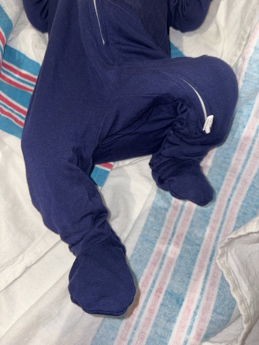 A baby dressed in a navy blue footed onesie lies on a striped blue, red, and white blanket. The post references a ticker symbol "$baby" with a 2044 expiration, using a play on words relating to the literal baby in the image alongside the financial term "premarket."