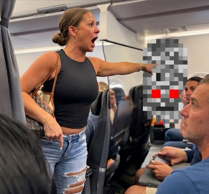 A woman with a blonde bun, wearing a black tank top and ripped jeans, angrily points and shouts at a man in a blue shirt seated on an airplane, while other passengers look on. The post's claim that the dispute involves a "ghost" from @CRTGhosts appears to be a joking reference to the in-flight altercation, with the pixelated figure in the background possibly meant to humorously represent the "ghost" in question.