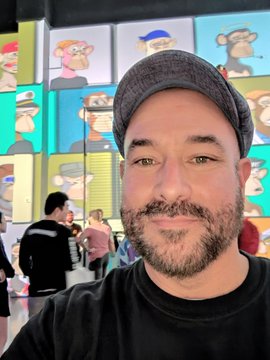The image features a man wearing a hat, standing next to a wall with various cartoon characters displayed behind him. The caption for this image reads "I am a Bored Ape. I am part of the best Club on the internet. I celebrate the community we've built. I am proud to be a member of the Club." This post seems to be related to the man's hat and his affiliation with the cartoon character club, as he is wearing a hat that resembles one of the characters displayed behind him.