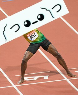 An athlete in a green and yellow top with the bib number '5001' is in a starting position on a red running track, with a white sign displaying a sad face emoticon drawn on it.