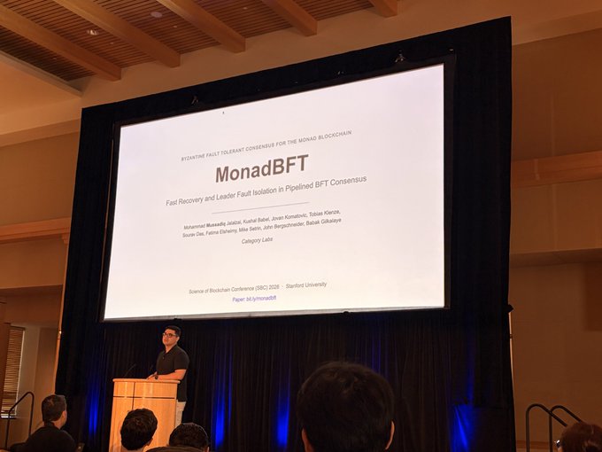 A man giving a presentation at a podium in front of a screen displaying a paper titled 'MonadBFT' from the Science of Blockchain Conference (SBC) 2028 at Stanford University.