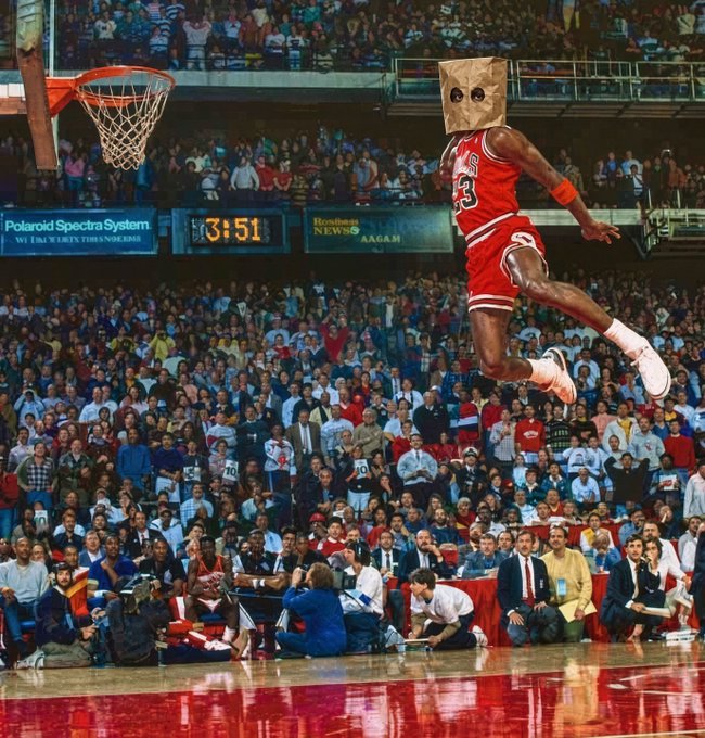 Michael Jordan, wearing his iconic red Bulls #23 jersey, soars through the air during the slam dunk contest, with a paper bag photoshopped over his head and a Polaroid Spectra System ad visible courtside.