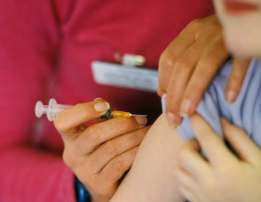 A close-up photograph of a healthcare worker in a red uniform administering a syringe injection into a patient's arm.