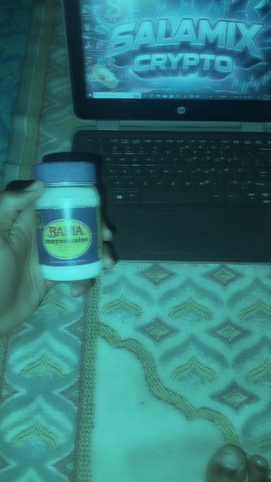 A hand holds a bottle labeled 'BA JA Mayonnaise' in front of a laptop displaying 'SALAMIX CRYPTO' on its screen.
