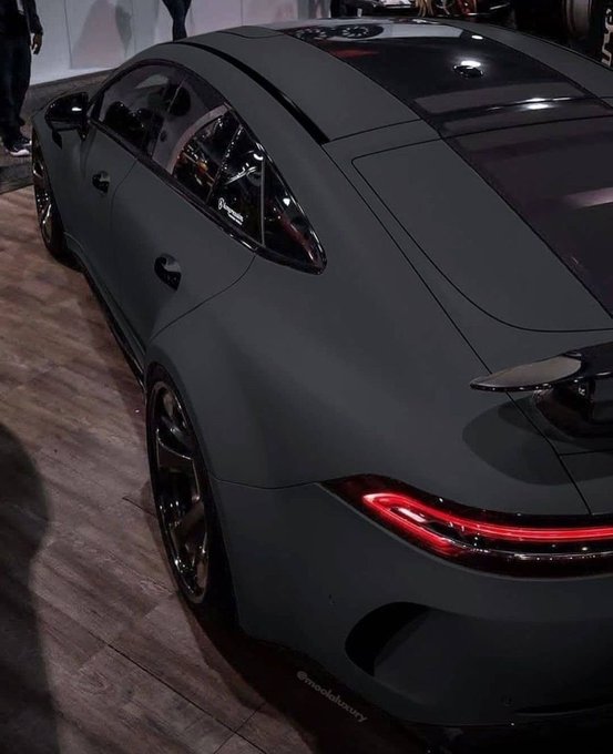A matte black Porsche 911 GT3 with illuminated red taillights and a rear spoiler is displayed on a wooden floor, likely at an auto show, with a watermark reading "@mr.elektrofory" visible at the bottom. The post humorously suggests wanting to purchase the luxury sports car using the $stkr cryptocurrency, with the sleek vehicle serving as the object of the poster's desire.