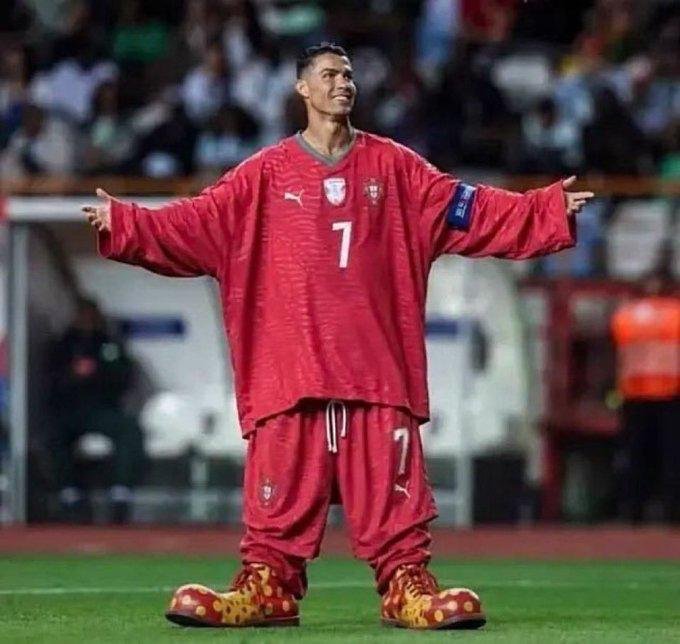 Soccer player Cristiano Ronaldo stands on a field wearing a red Portugal #7 jersey with his arms outstretched, paired with distinctive yellow and red Crocs shoes.