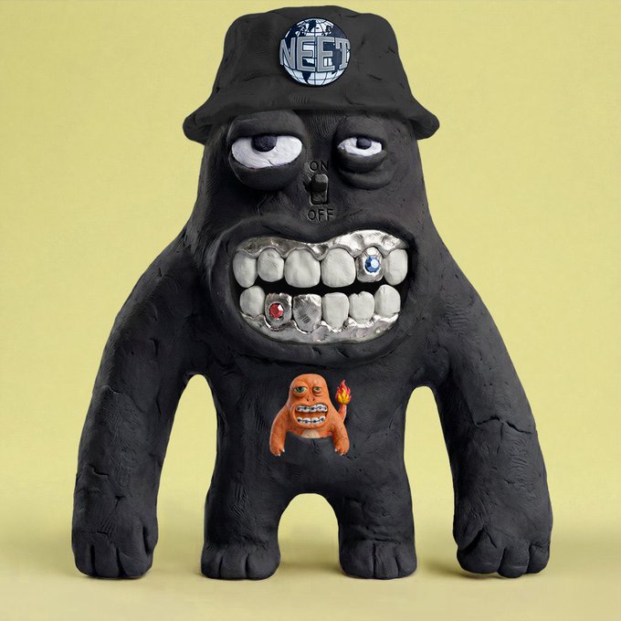 A black, monster-like figurine wearing a 'NEFT' cap, featuring an on/off switch on its face, a wide mouth full of jeweled teeth, and a small orange character on its stomach.