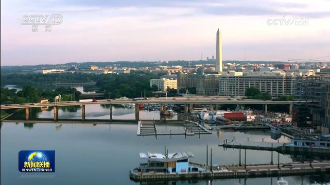 A CCTV 13 news broadcast (新闻联播, XINWEN LIANBO) showing an aerial view of Washington D.C., featuring the Washington Monument and a bridge over the Potomac River.