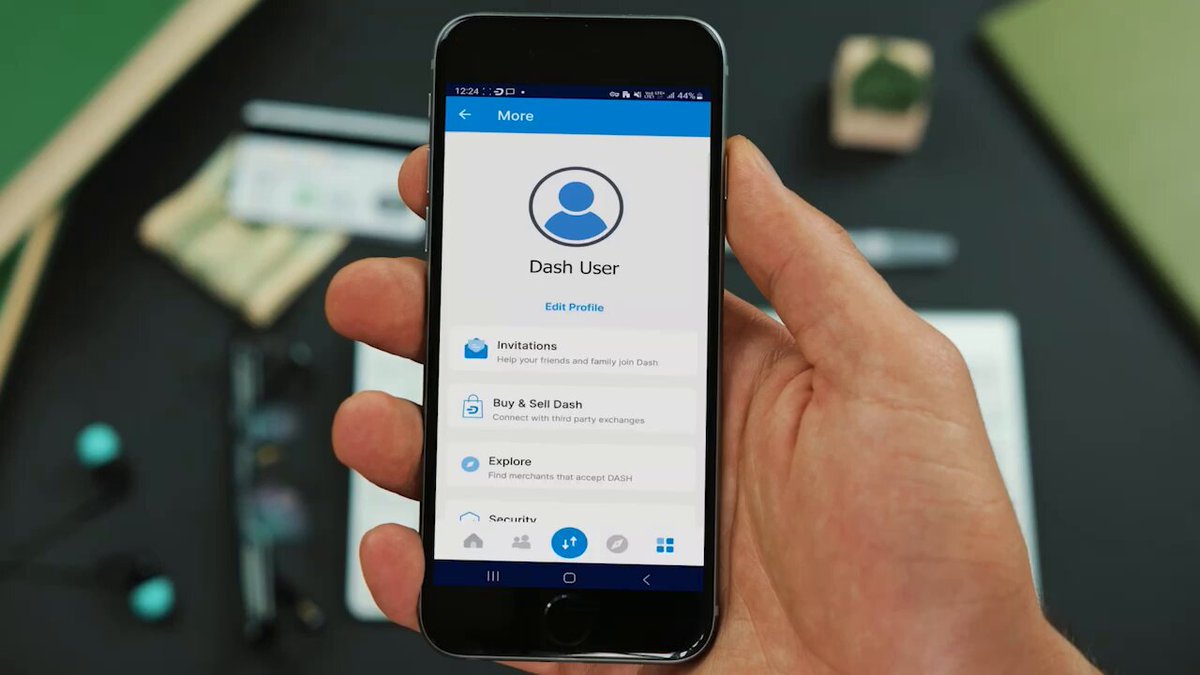 The image shows a person holding a smartphone displaying an app called "DashPay", which appears to be related to recurring purchases or payments. The phone's screen displays a blue icon with a white profile picture of a person, indicating that this app is designed for managing recurring transactions. The person holding the phone seems to be interested in using the DashPay app and might be considering setting up a recurring payment system for their expenses.