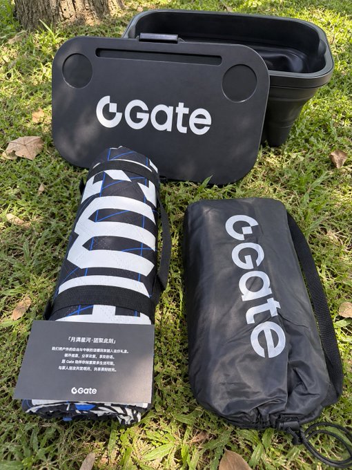 A collection of outdoor gear branded with 'GGate' is laid out on grass, including a black storage box, a rolled-up striped mat, a black carrying bag, and a small information card.