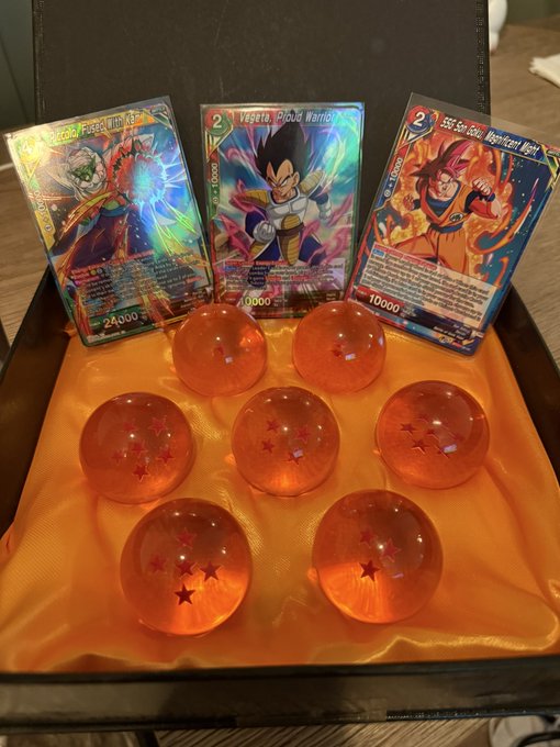 A black box holds six orange dragon ball figurines, accompanied by a blue and white card with a dragon character on it.